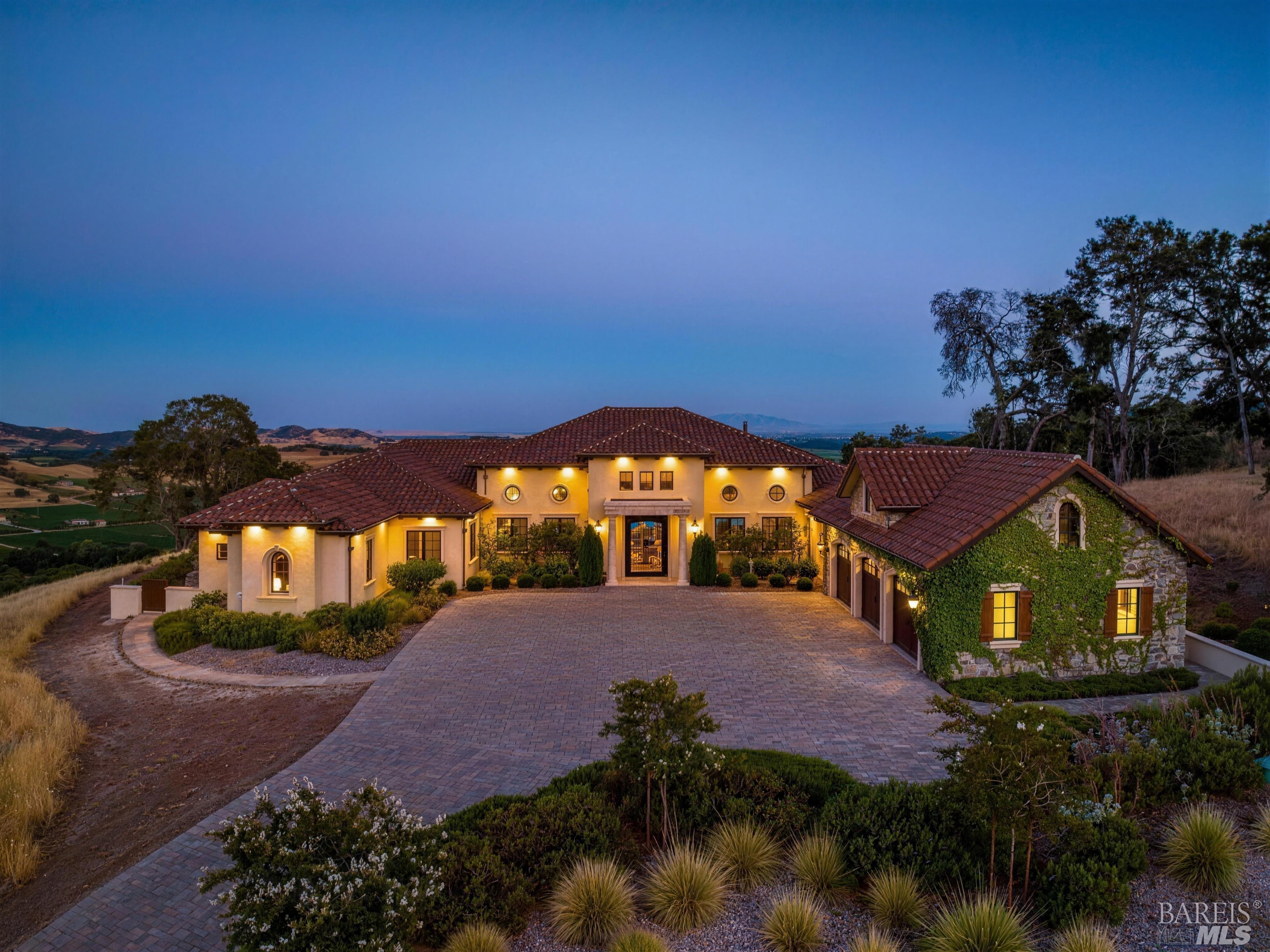 A Tuscan-inspired hilltop villa lit from within at dusk, above Suisun Valley vineyards